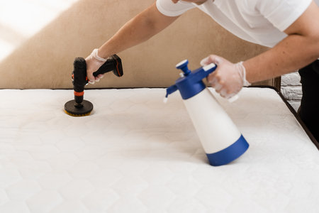 Spraying and smearing detergent on white mattress using drill with brush for dry cleaning. Applying detergent on mattress for dry cleaningの写真素材