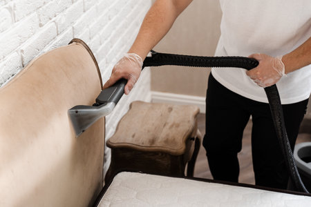 Dry wash cleaner is removing dirt and dust from bed headboard using dry cleaning extraction machine. Process of extraction dirt from headboard of bed using extractor cleaning machineの写真素材