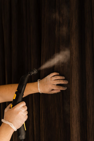 Close-up curtains dry wash using steam machine at home. Steaming of textile curtain. Process of disinfection and dry cleaning of curtains at homeの写真素材