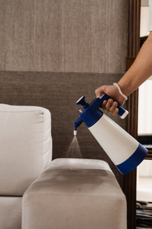 Spraying detergent on couch for dry cleaning using extractor machine. Process of dry cleaning for removing stains and dirt from couch at home. Professional cleaning serviceの写真素材