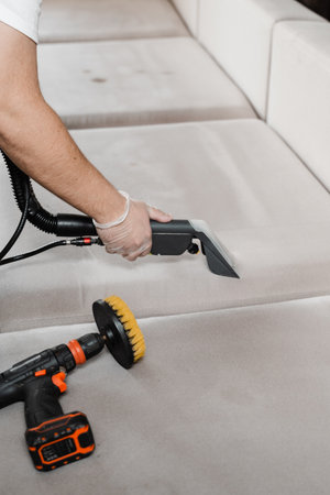 Housekeeper is extracting dirt from upholstered sofa using dry cleaning extraction machine. Cleaner is cleaning couch with washing vacuum cleaner extractor machine for dry clean upholstered furnitureの写真素材