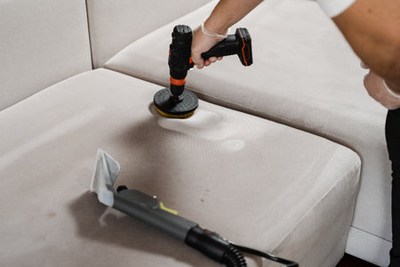 Smearing detergent on couch using drill with brush for dry cleaning. Applying detergent on sofa in home interior for dry cleaningの写真素材