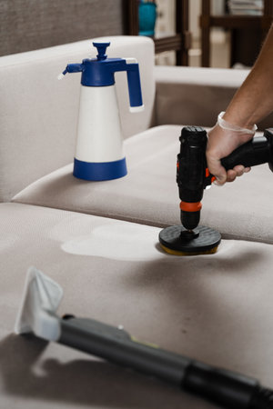 Smearing detergent on couch using drill with brush for dry cleaning. Applying detergent on sofa in home interior for dry cleaningの写真素材