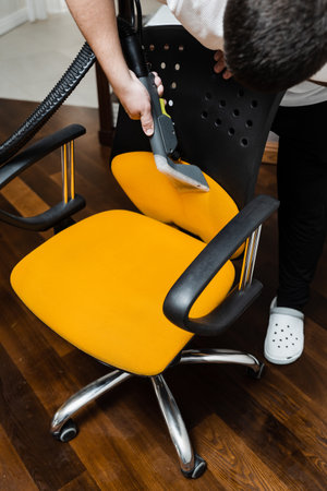 Housekeeper is extracting dirt from yellow armchair using dry cleaning extraction machine. Cleaner is cleaning chair with washing vacuum cleaner extractor machine for dry clean upholstered furnitureの写真素材