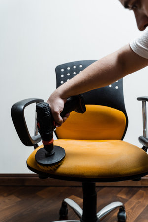 Smearing detergent on armchair using drill with brush for dry cleaning. Applying detergent on chair...