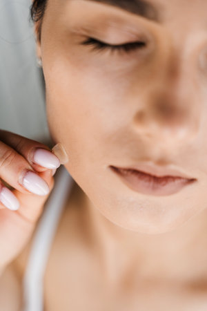 Applying acne round patch on cheek of girl close-up. Young woman using acne patches for treatment of...