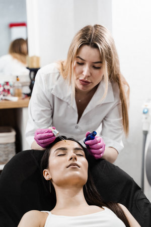 Dermatologist is applying moisturizing serum on face of model. Cosmetologist is applying hyaluronic...