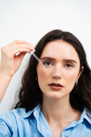 Girl is applying hyaluronic serum with pipette on face. Young woman with acid dropper is applying drops of acid on her skinの写真素材