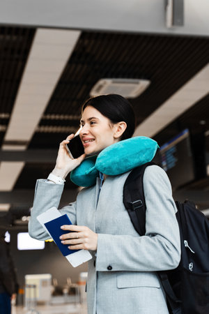 Asian girl with neck pillow is talking on smartphone in airport waiting room during boarding. Young...