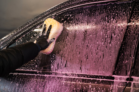 Cleaning the vehicle side window using a sponge and detergent during manual vehicle washing at a...