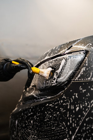 Manual cleaning with soap at self care car wash. Cleaning headlights with foam and soft brush. Carwash and detailingの写真素材