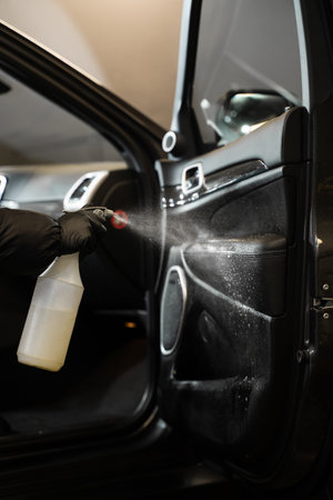 Professional vehicle detailing at car wash service. Applying spray detergent on car door. Cleaning and disinfecting car salonの写真素材