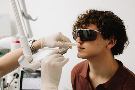 Laser treatment inflammation of the nasal lining, runny nose, sneezing symptoms. Laser treatment of chronic rhinitis. ENT doctor with laser treats man patient in protective glassesの写真素材