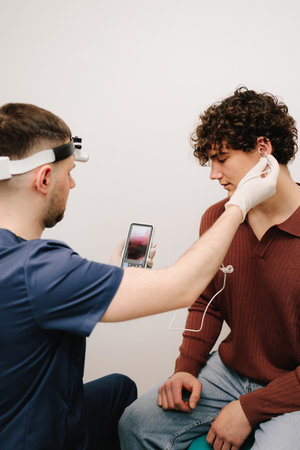 ENT doctor is making checkup of male patient ear with digital otoscope. Man patient and ENT doctor...