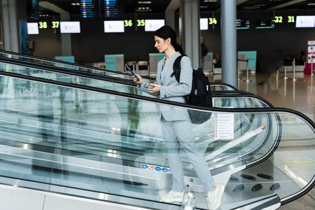 Business woman on the escalator at the airport is going to flight abroad. Tourist with backpack...