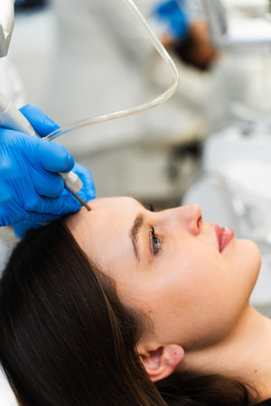 Laser removing moles and birthmarks from face of attractive girl. Cosmetologist applies laser device...