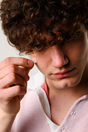 Using acne pimple patch to clean the face from zits. Young man uses acne stickers as bandage not to...