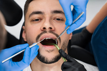Handsome man is having preventive dental checkup in clinic. Initial examination of the patients oral...