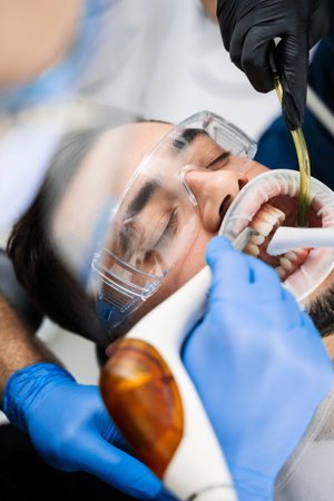 Assistant helps dentist to prepare teeth before treatment using airflow instrument. Airflow teeth...
