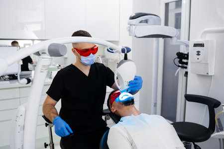 Patient whitens his teeth wearing goggles and lip retractor. Dental whitening procedure by ultraviolet lightの写真素材