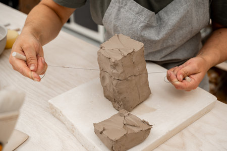 Slicing off a chunk of clay from a large block using a sharp wire clay cutter. Using a wire cutter...
