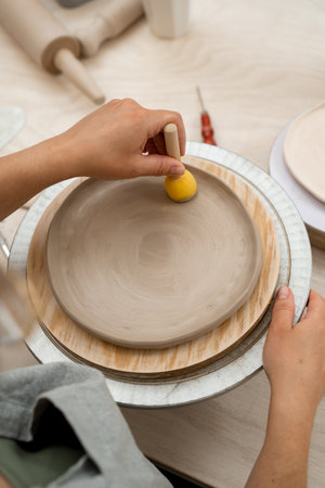 Girl is working with a sponge on a stick to shape pottery and absorb excess water from clay. Using...