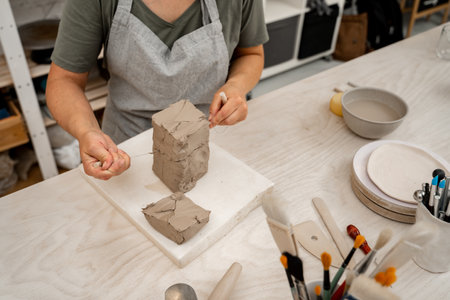 Girl is using a wire cutter to cut off a piece of clay before modeling the product. Slicing off a...