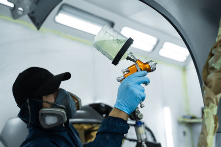 Putting lacquer on metal to give surface smooth appearance. Worker wearing protective mask and...