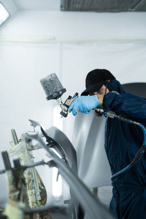 Car painter is changing the color of vehicle using sponge and paint sprayer. Worker is painting car in dark color with HVLP spray gunの写真素材