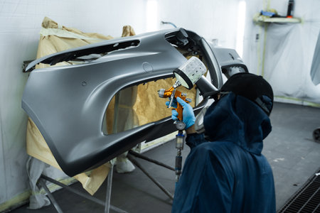 Car painter is applying lacquer on car using LVLP spray gun. Putting lacquer on metal to give surface smooth appearanceの写真素材