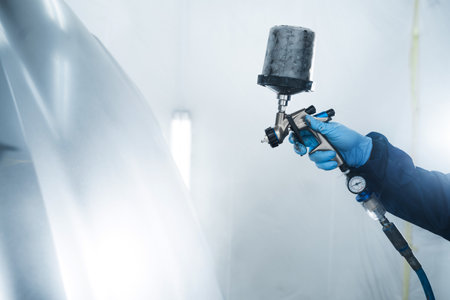 Car painter is using HVLP or LVLP spray gun to apply paint on metal. Painting cars in vehicle maintenance service using paint sprayerの写真素材