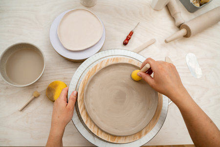 Using wooden handle sponge to smooth the surface of a clay product in a pottery workshop. Working with a sponge on a stick to shape pottery and absorb excess water from clayの写真素材