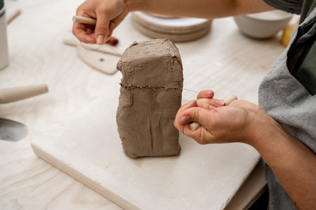 Girl is using a wire cutter to cut off a piece of clay before modeling the product. Slicing off a...