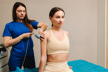 Diathermy. Doctor is doing tecar therapy to female patient to heal her injured shoulder. Using high frequency currents to reduce pain and assist recovering body tissuesの写真素材