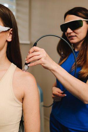 Arm laser therapy. Helping to relieve pain and inflammation with infrared light. Doctor wearing protective glasses is doing laser therapy on arm to patientの写真素材