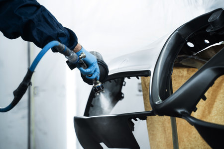 Worker is painting car in dark color with HVLP spray gun. Auto mechanic is changing the color of vehicle using sponge and paint sprayerの写真素材