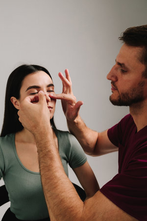 Rhinoplasty. Surgeon is taping nose to patient during rhinoplasty recovery. Applying bandage on nose after surgery to support its shape, decrease swelling and improve appearanceの写真素材