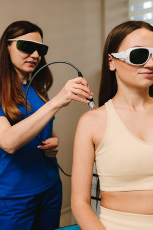 Arm laser therapy. Doctor wearing protective glasses is doing laser therapy on arm to patient. Helping to relieve pain and inflammation with infrared lightの写真素材