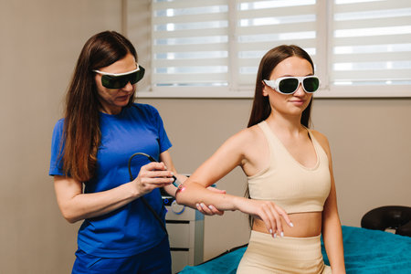 Arm laser therapy. Doctor wearing protective glasses is doing laser therapy on arm to patient. Helping to relieve pain and inflammation with infrared lightの写真素材