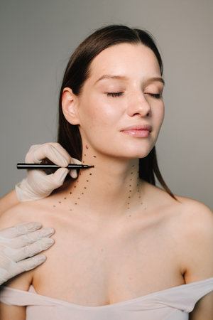 Cosmetologist is drawing dotes before botulinum toxin injection in platysma of a woman. Mark up before Nefertiti lifting. Improving neck by a professional. Female aesthetic cosmetologyの写真素材
