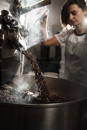Coffee roaster checks freshly roasted coffee beans in the factory. Organic coffee grains in the special equipment. Roasted coffee beans productionの写真素材
