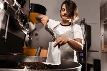 Worker pouring roasted coffee beans in packaging bag. Filling coffee grains in a craft bag. Packing fried coffee beansの写真素材