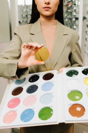 Selecting eye lens after optic checkup. Large selection of colorful lenses for eyesight correction. Female client holds colorful optical lens in the optical storeの写真素材