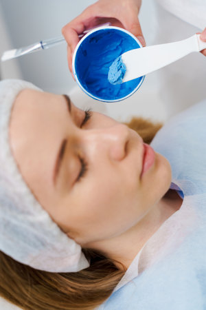 Applying face mask for skincare wellnesses and humidification in spa. Getting facial treatment for a women with moisturizing mask by cosmetologistの写真素材