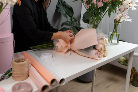 Florist ties a flower arrangement with the ribbon to the order in the flower shop. Making fresh bouquet from roses for the deliveryの写真素材
