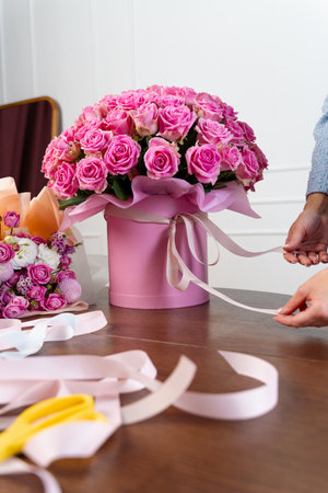 Packing bloom composition of roses to the customers. Process of bouquet designing in the floral shop. Florist ties a bouquet of pink roses with white ribbon in the flower storeの写真素材