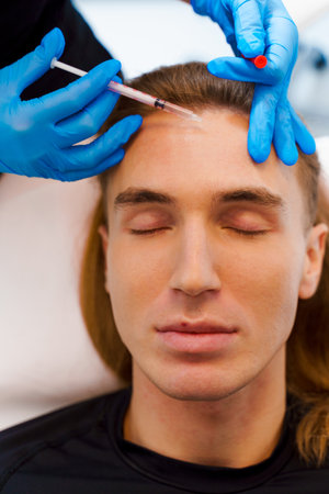 Botulinum toxin injection procedure on the man's forehead in the beauty center. Filler injection...