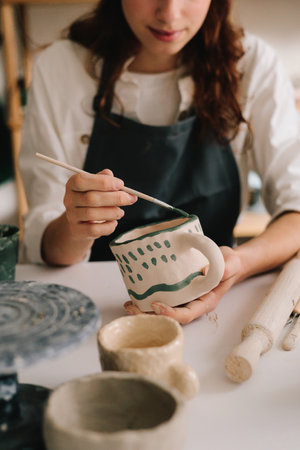 Potter draws an abstract design into earthenware cup. Experienced artist painting designs on ceramic...