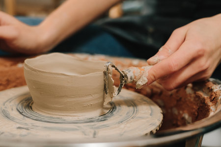 Creating ceramic earthenware on the manufacturing. Artisan forms clay pot with potters tool on the...