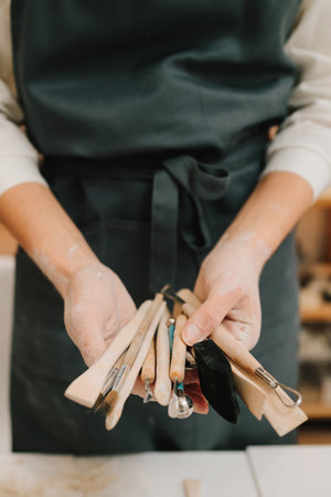 Potter holds craft instruments for clay sculpting. Wooden craft tools for molding ceramic crockery